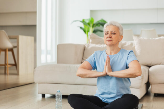 Yoga mindfulness meditation. Senior adult mature woman practicing yoga at home. Mid age old lady sitting in lotus pose on yoga mat meditating relaxing, Older middle aged woman doing breathing practice