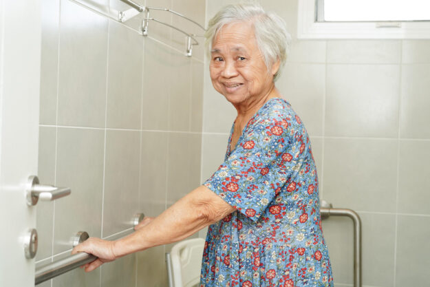 Asian elderly old woman patient use toilet support rail in bathr