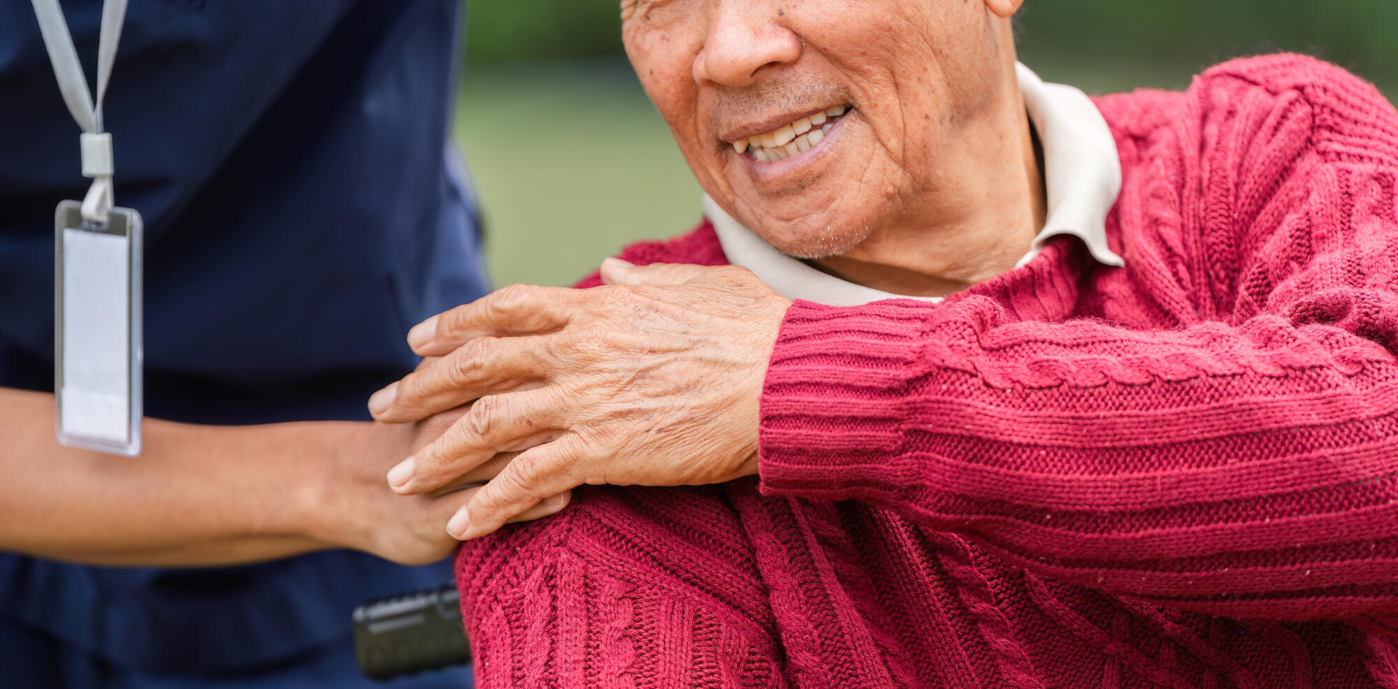 Close-up of elderly man’s joyful smile with caregiver’s hand providing gentle support in the garden