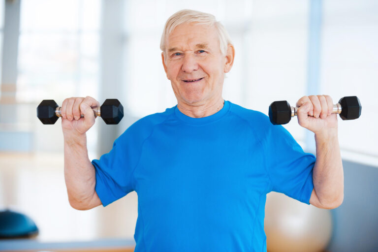 Staying healthy. Happy senior man exercising with dumbbells and smiling while standing indoors