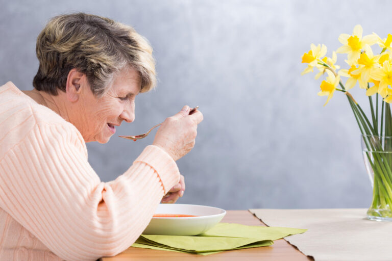 Senior,Woman,Sitting,Beside,Table,,Eating,A,Soup
